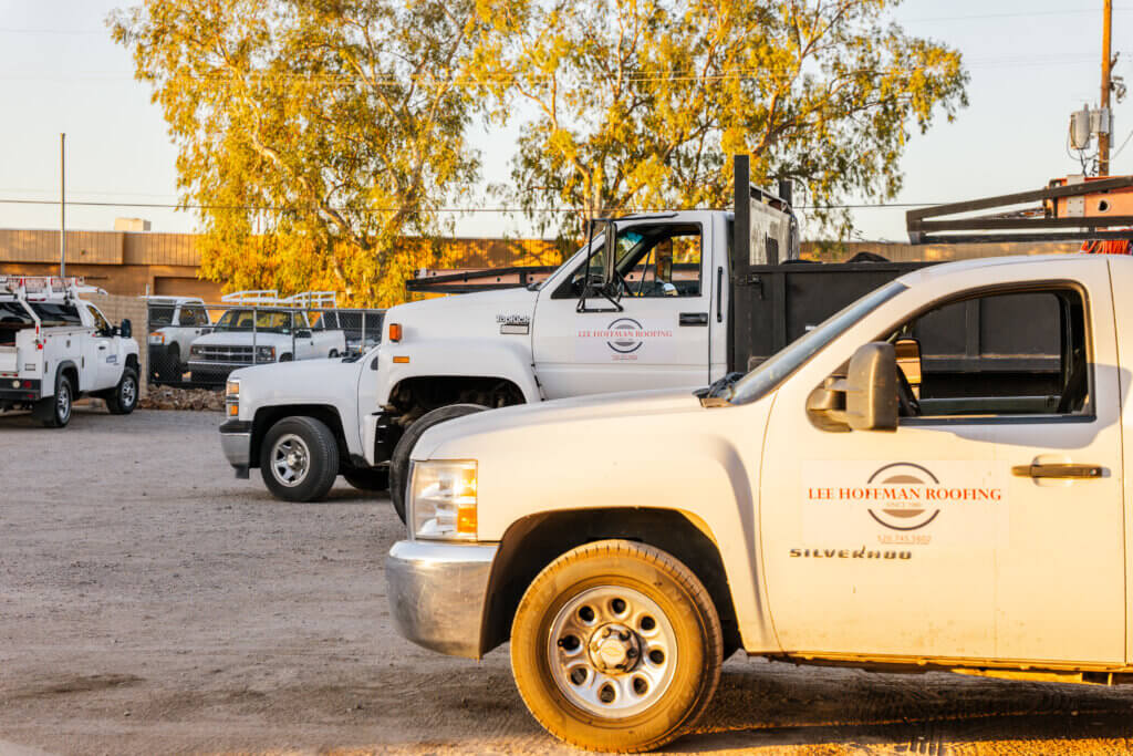 Several white trucks are parked in the lot at a roof restoration business in Tucson