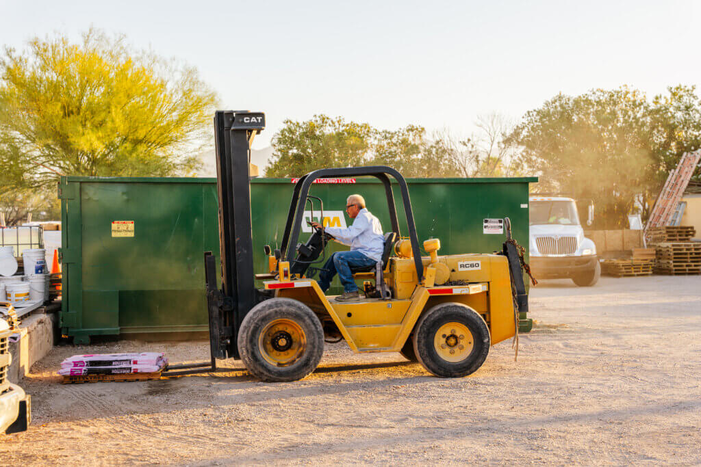 A roofing contractor is using a forklift to transport roofing materials on a jobsite where they are performing roof repair services