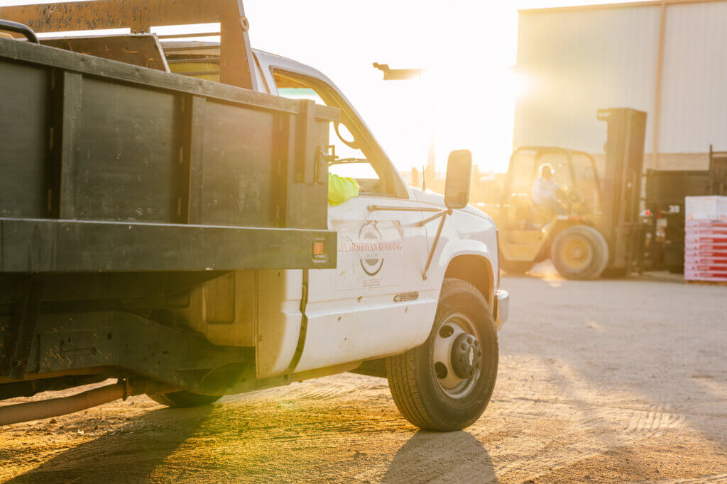 A truck is pulling into a warehouse area where a forklift is moving roofing materials to prepare for a new roof project