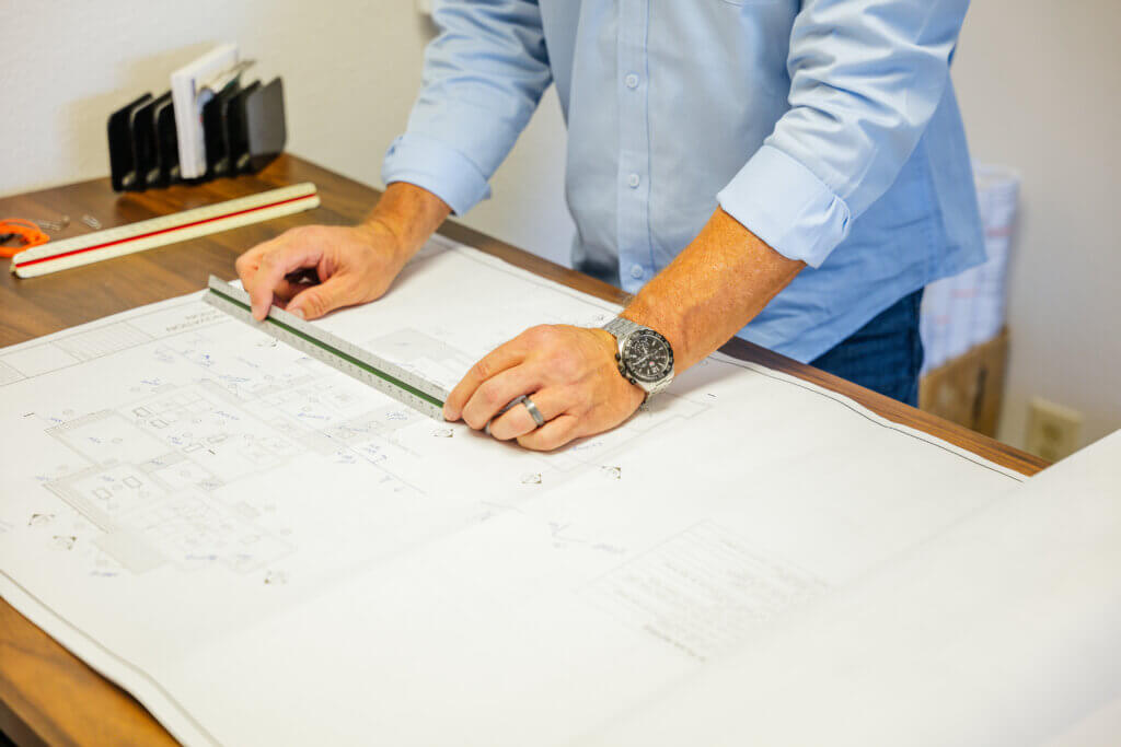 A roofing contractor is using a ruler to measure the blueprints for a home as they prepare for a new roof installation