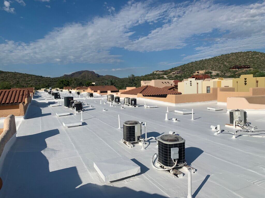 A large, flat commercial roof that has recently had a white roof coating applied with mountains and the Tucson countryside in the background